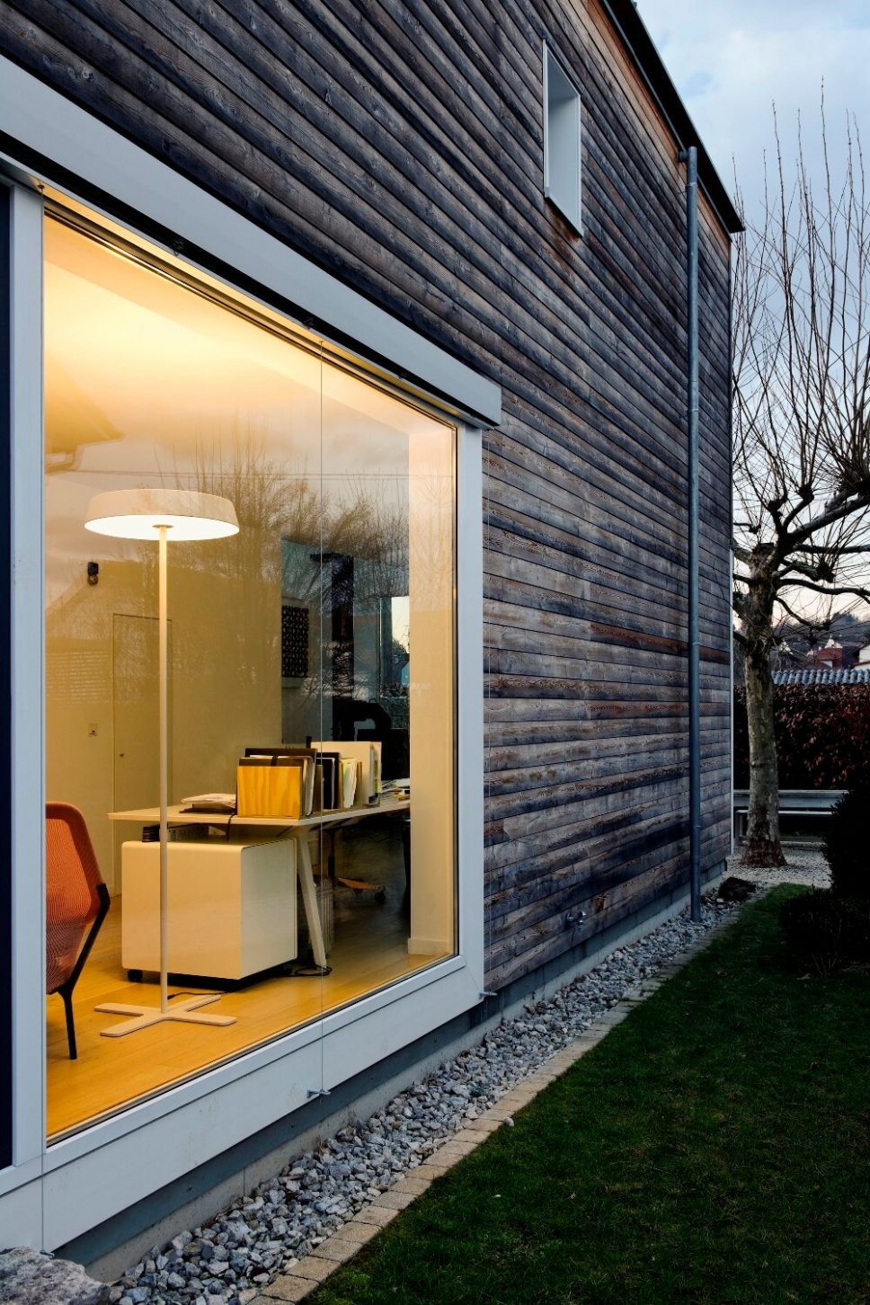 Blick durch ein Panoramafenster zeigt Home Office mit Stehleuchte