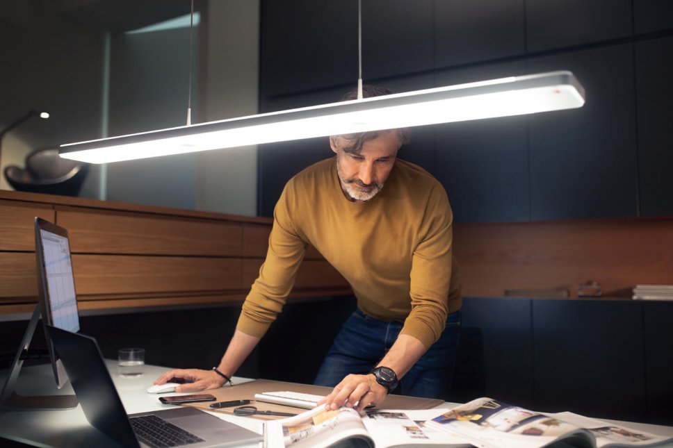 Moderne Pendelleuchte hängt über Schreibtisch, Mann arbeitet darunter