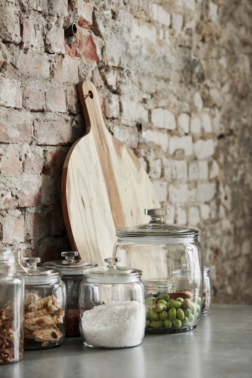 Vorratsgläser und Holzbrett vor Backsteinwand
