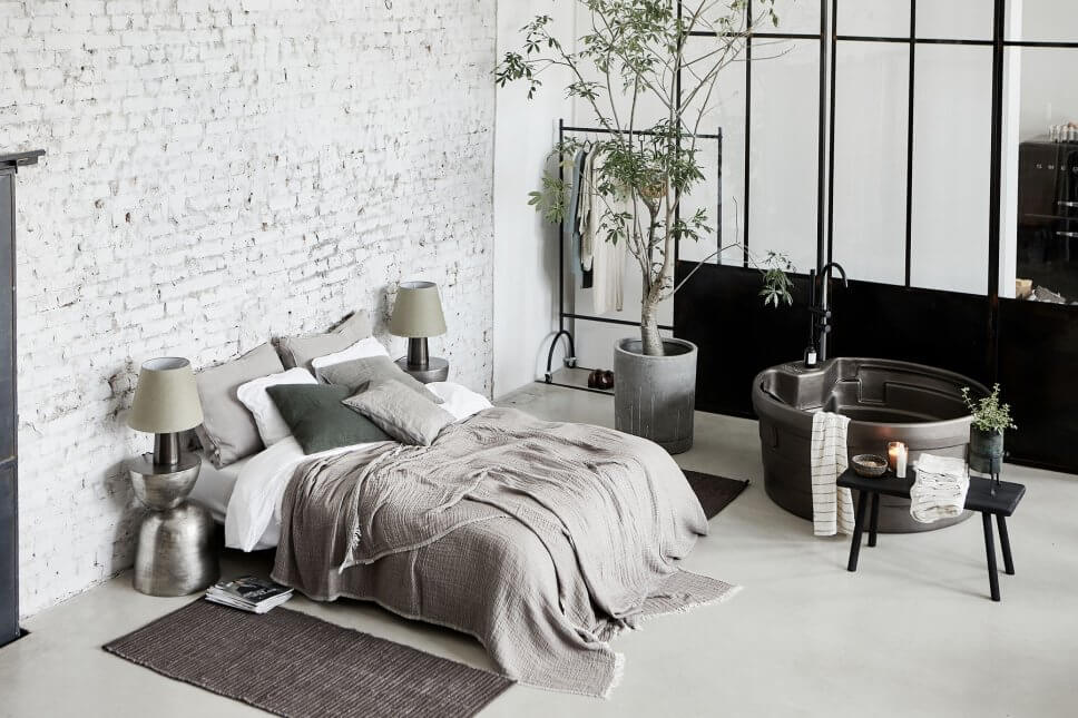 Bett vor Backsteinwand und freistehende Badewanne