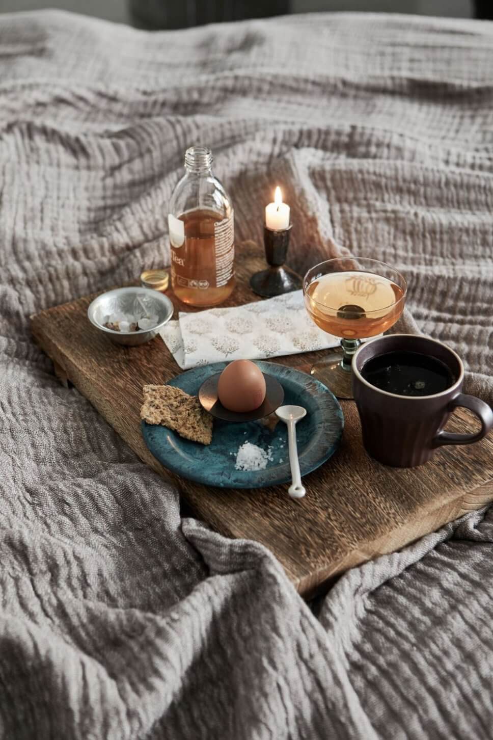 Holzbrett mit Teller und Frühstücksei sowie Kaffeebecher auf Bettdecke