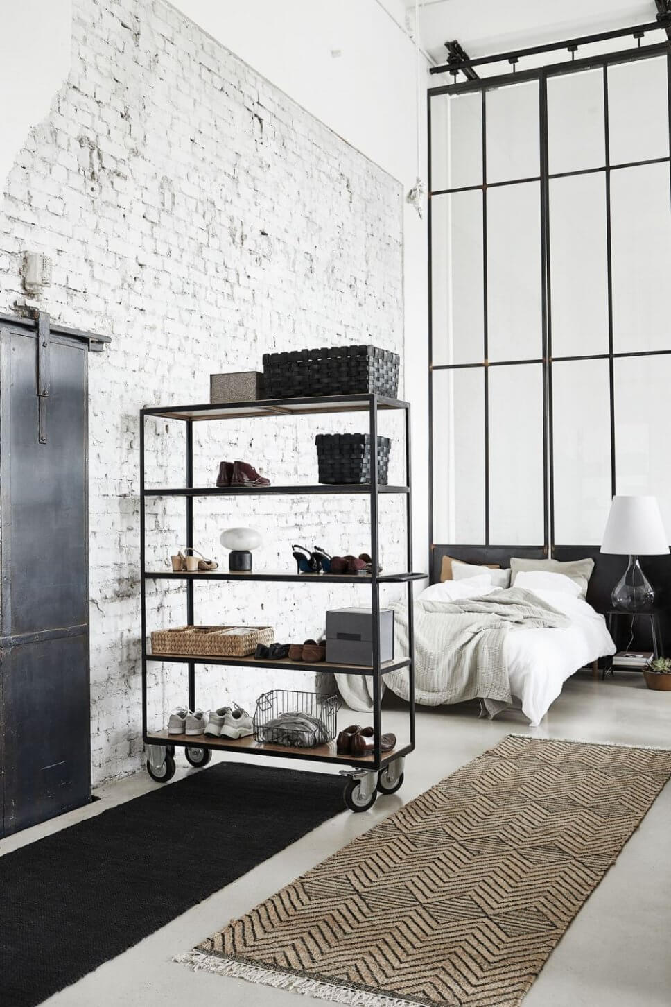 Stahlregal auf Rollen vor Bett neben Backsteinwand
