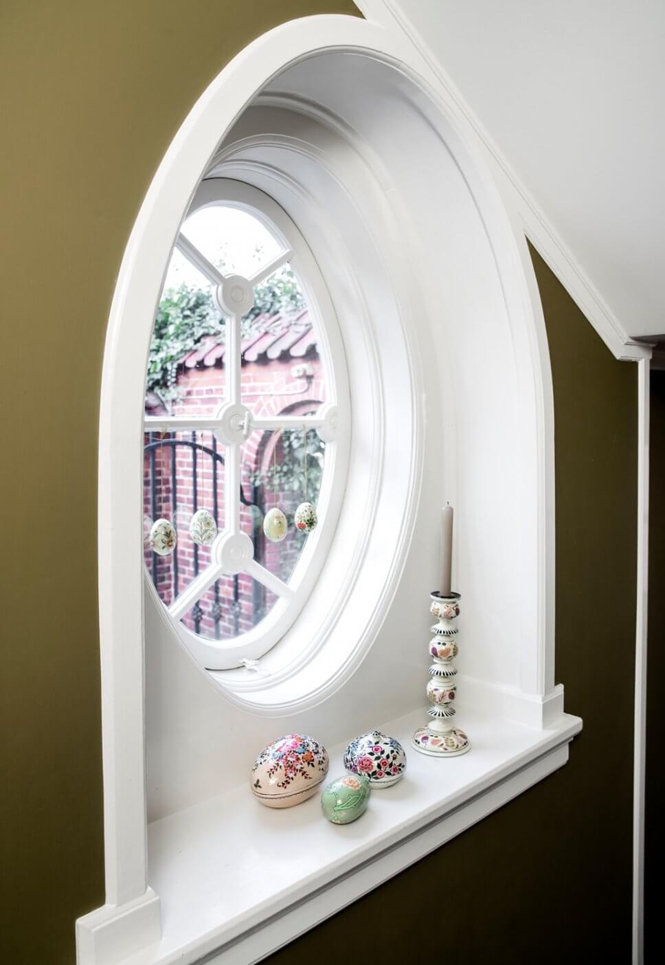 Ostereier hängen in rundem Altbaufenster, bemalte Holzeidosen liegen auf Fensterbank