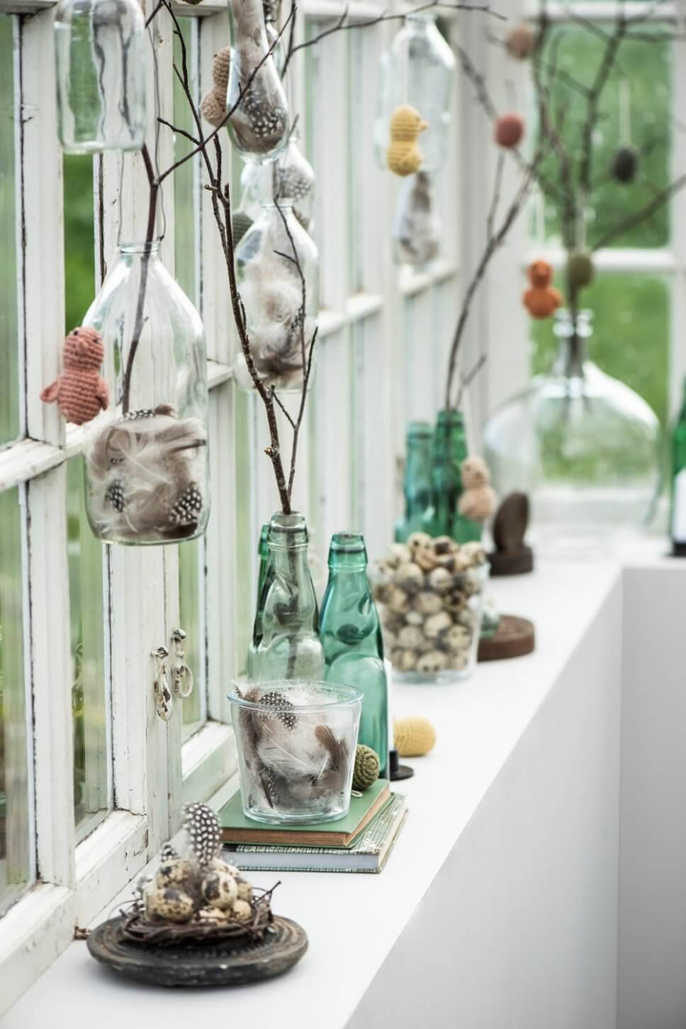 Gehäkelte Küken hängen an Zweigen in Flaschen auf Fensterbank