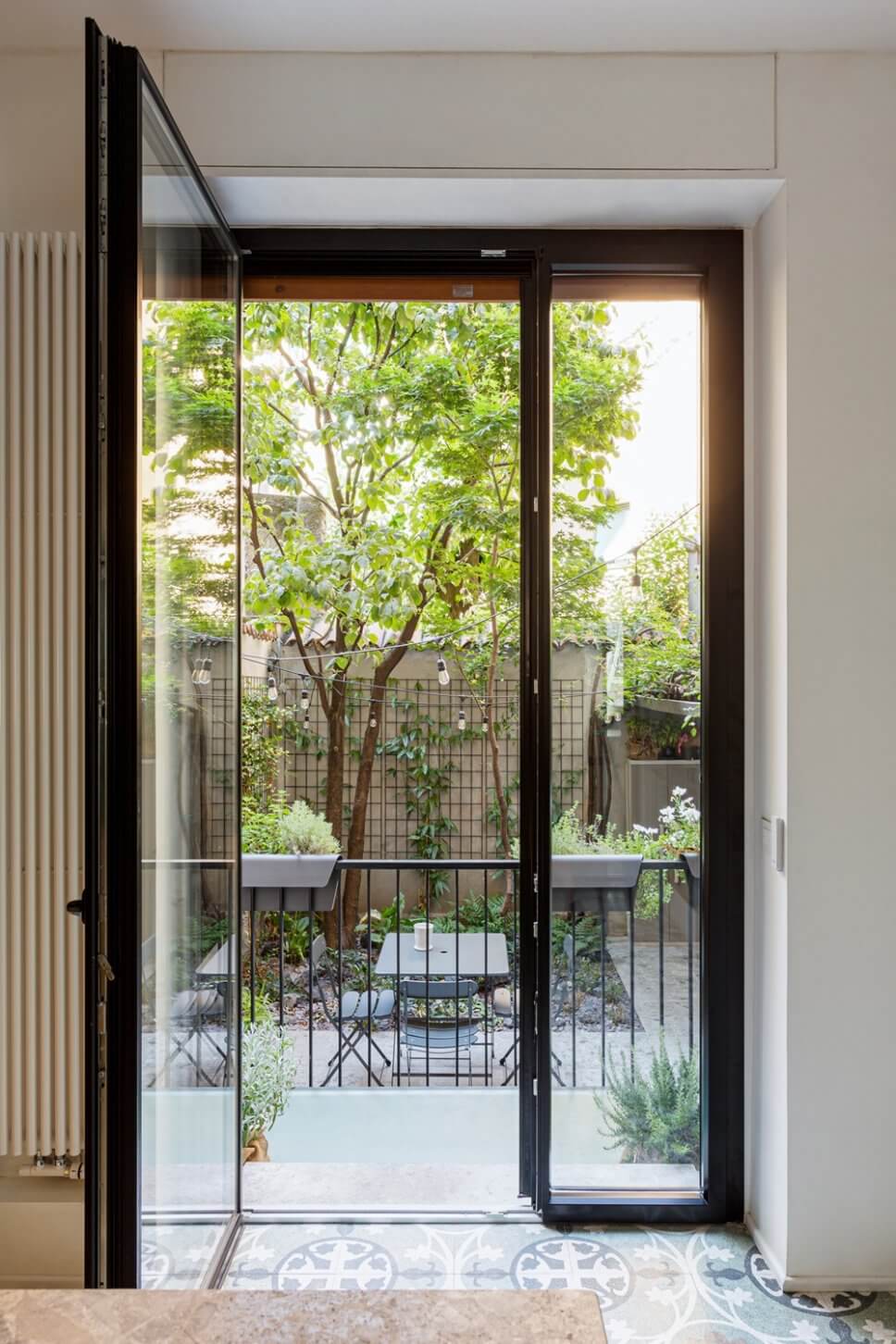 Geöffnete Balkontür mit Blick auf begrünten Innenhof mit Tisch-Stuhl-Ensemble