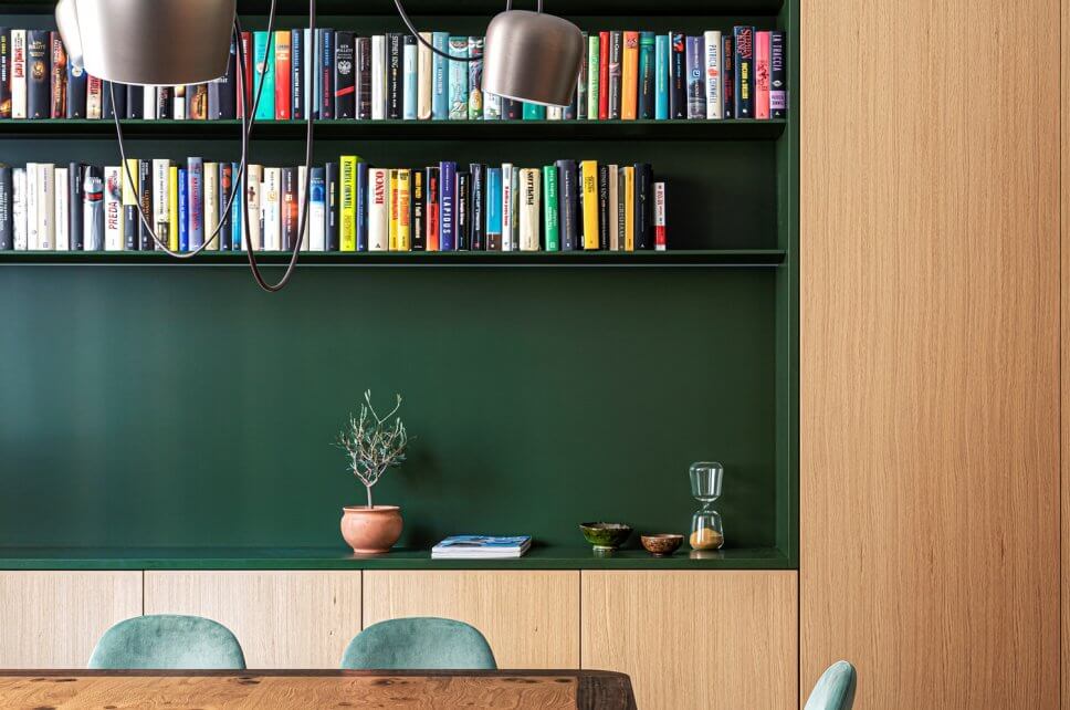Modernes Esszimmer mit Einbauschrank aus Holz und Bücherregal auf grünem Grund mit Holztisch und grüngrauen Samtstühlen