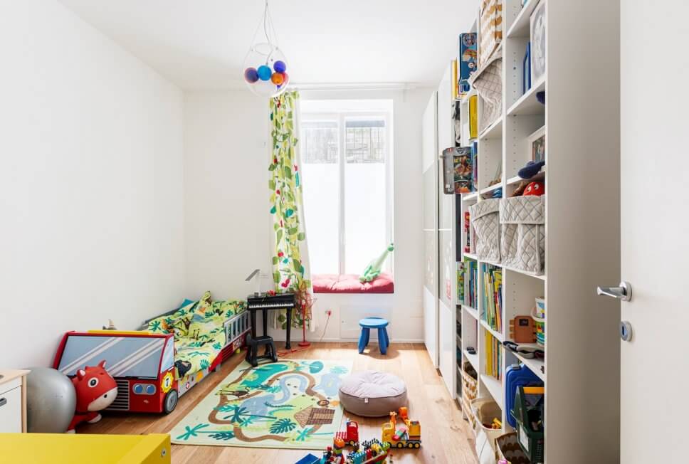 Buntes Kinderzimmer mit Bett in Form eines Feuerwehrautos, Regal, Schiebtürschrank und Spielzeug
