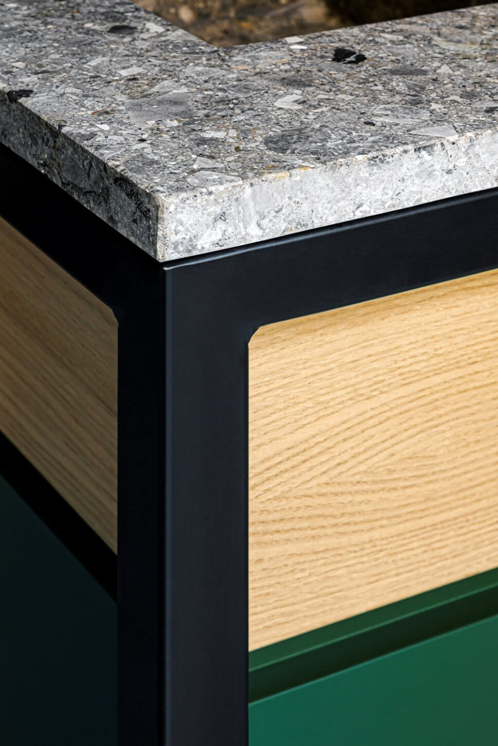 Detail einer Kücheninsel aus grauem Stein, hellem Holz und grünem Lack