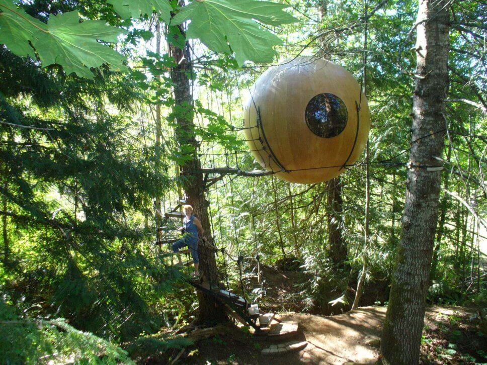 Großes Baumhaus aus Holz in Form einer hängenden Kugel im Wald