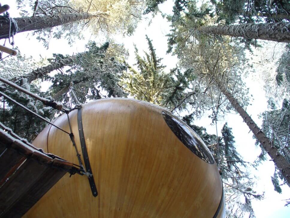Großes Baumhaus aus Holz in Form einer hängenden Kugel im Wald