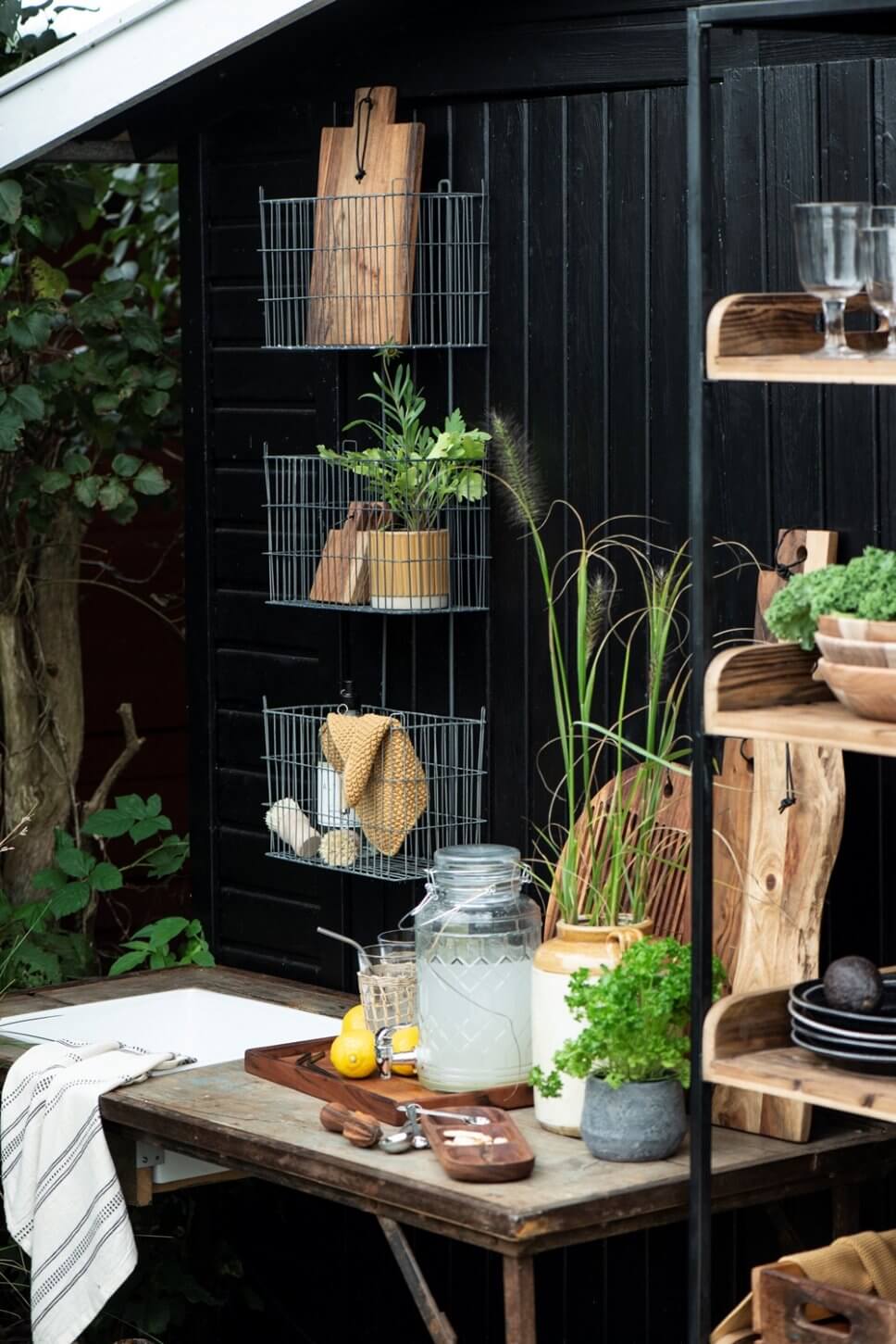 Rustikale Outdoorküche mit Holztisch, Metallregalen und vielen Kübelpflanzen