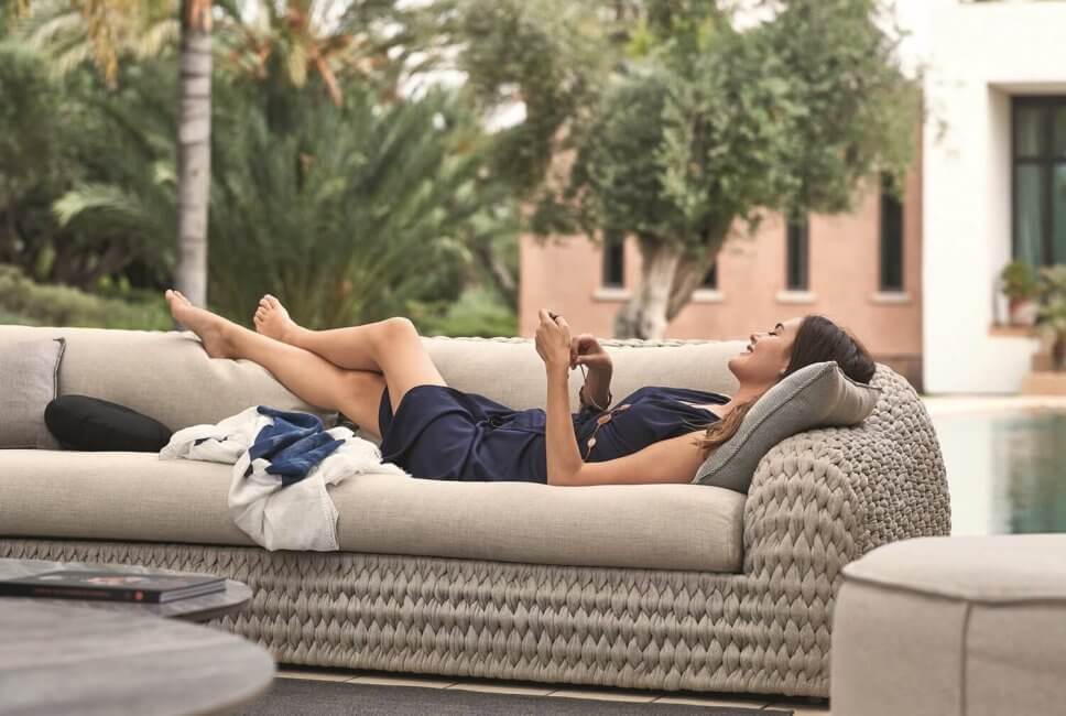 Frau liegt auf modernem Gartensofa auf Terrasse