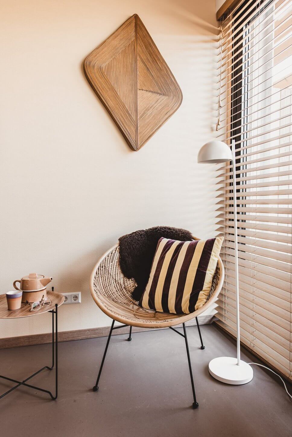Modern eingerichteter Wohnraum mit Korbsessel, auf dem ein gestreiftes Kissen und ein Schaffell liegen