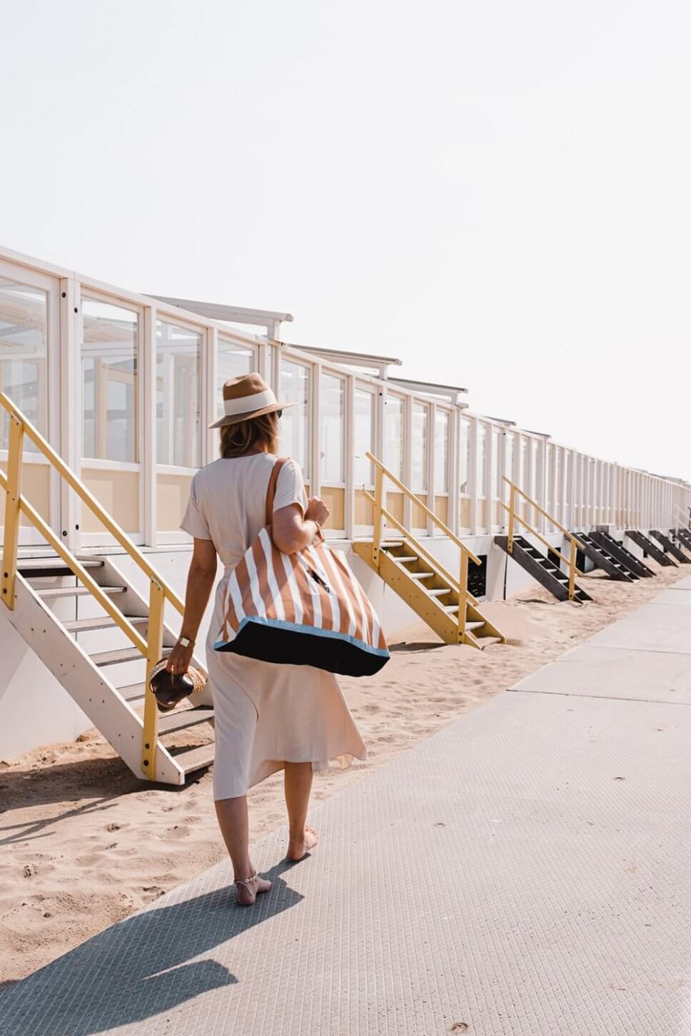 Frau mit einer Strandtasche über der Schulter geht an einer Reihe Badehäuser vorbei