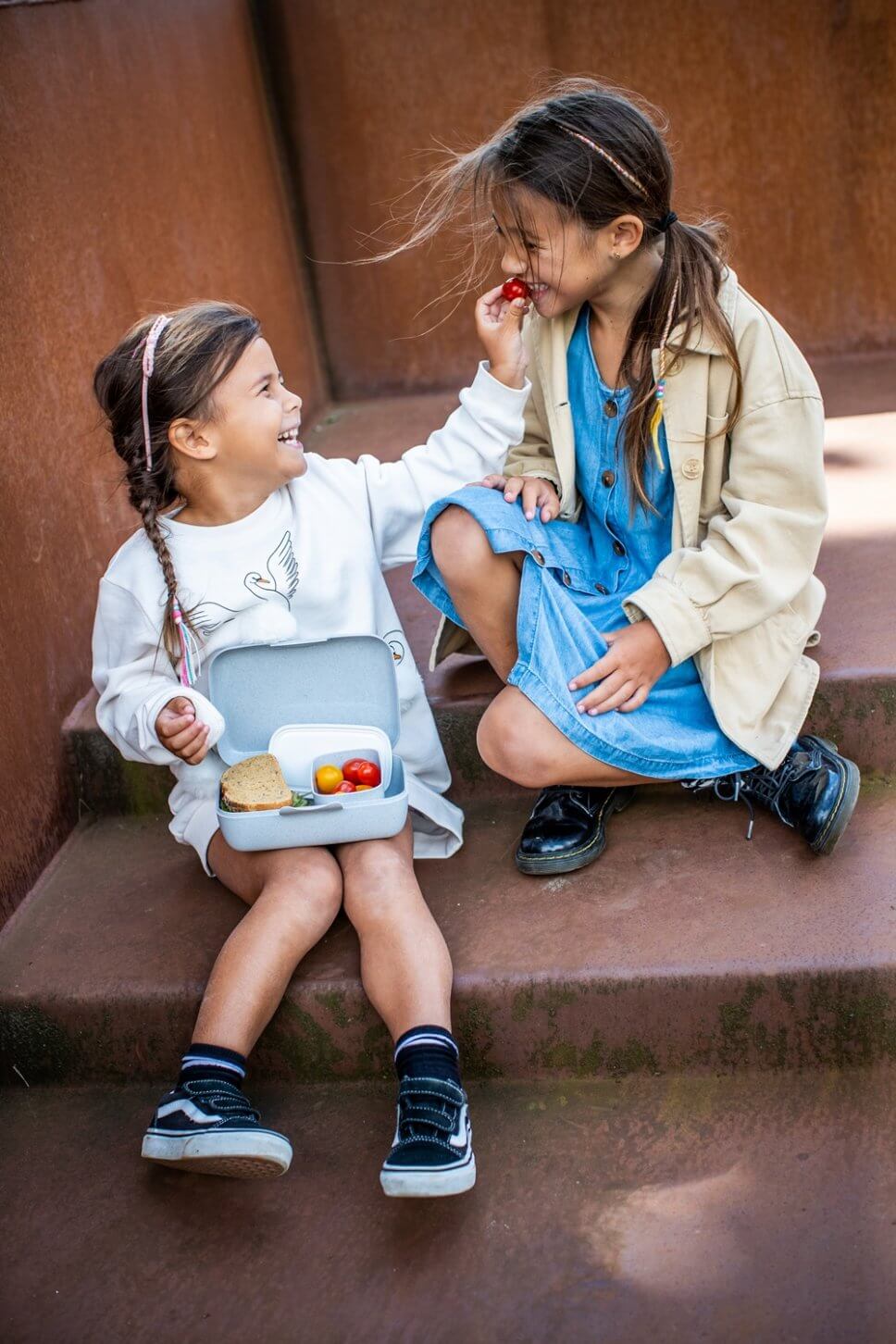 Zwei Mädchen sitzen mit einer Brotdose auf Stufen