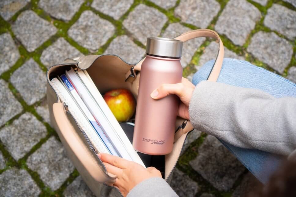 Hände stecken Thermosbecher in eien Schultasche