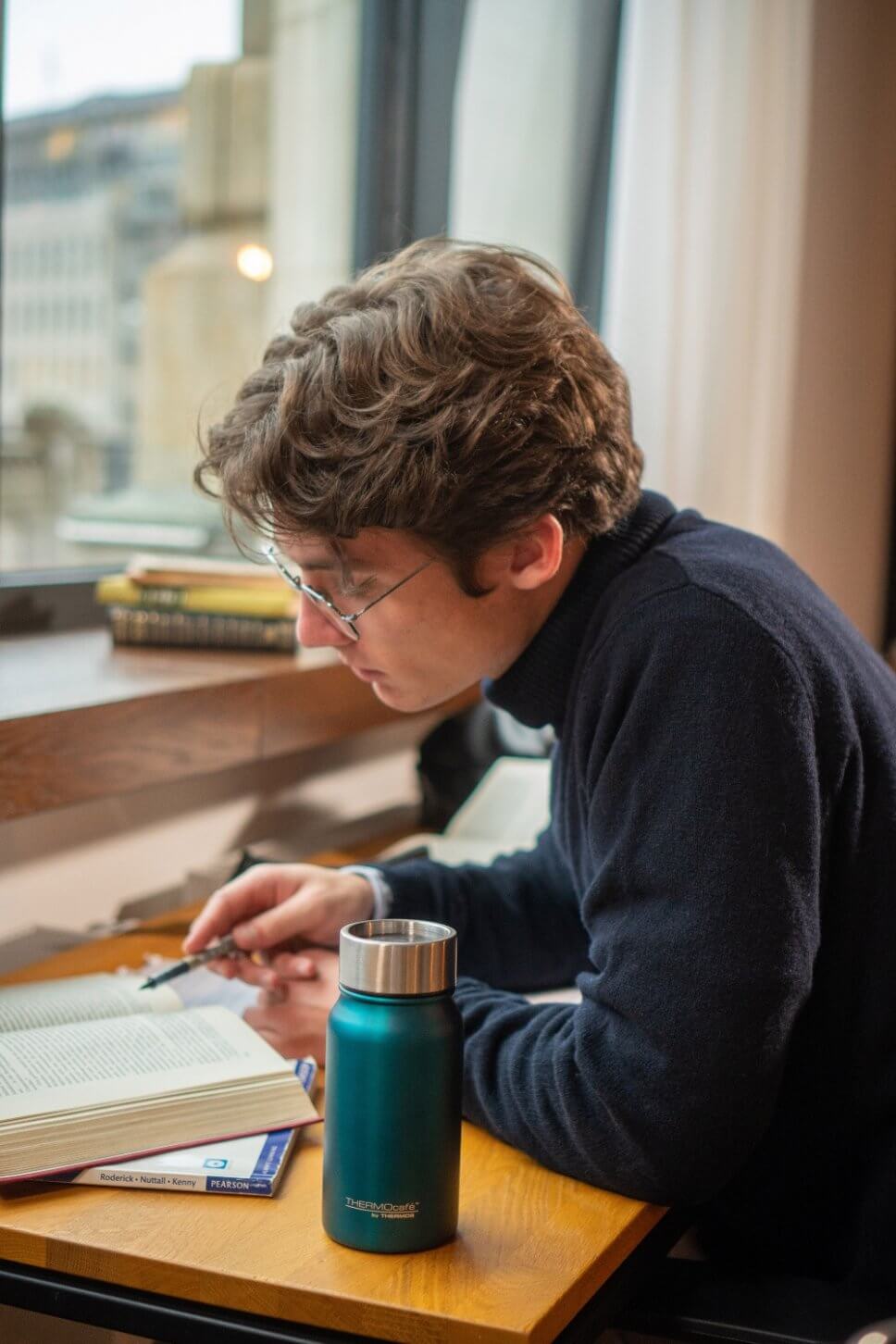 Junger Mann sitzt am Schreibtisch, darauf ein Thermosbecher