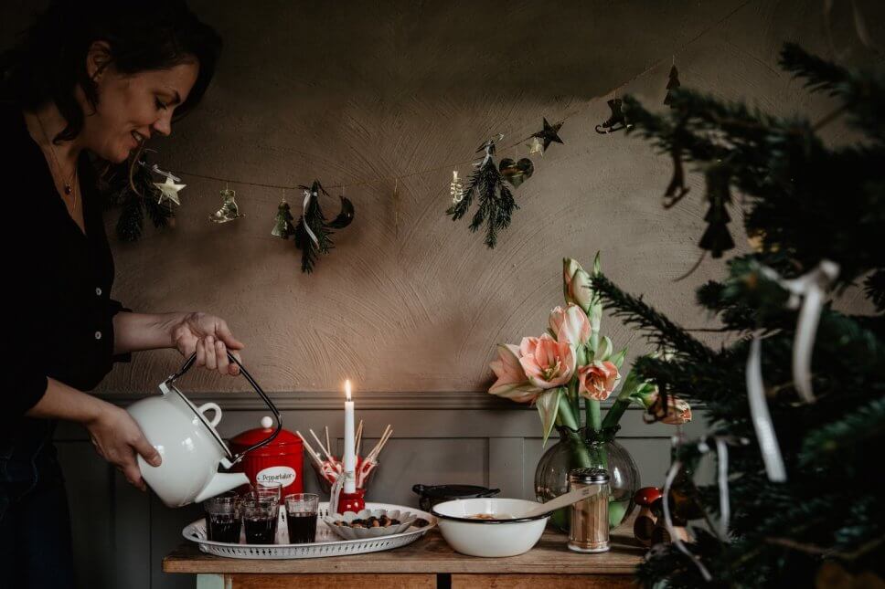 Frau schenkt Punsch ein im mit Weihnachtsdeko geschmückten Zimmer