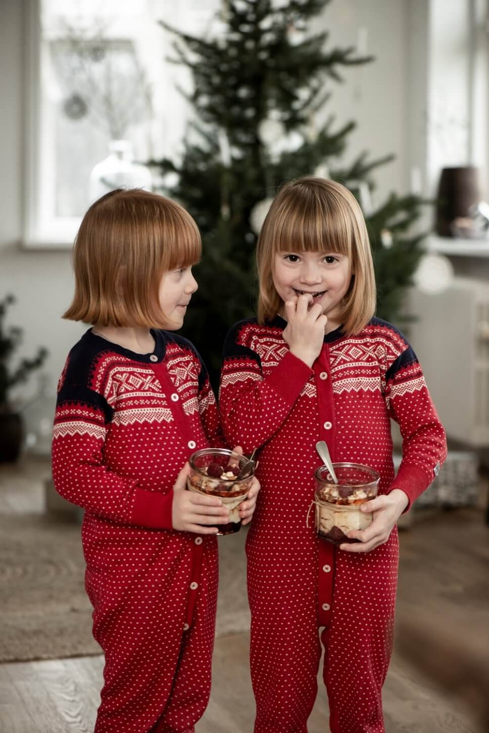Zwei Kinder stehen mit Nachtisch im Glas vorm Weihnachtsbaum