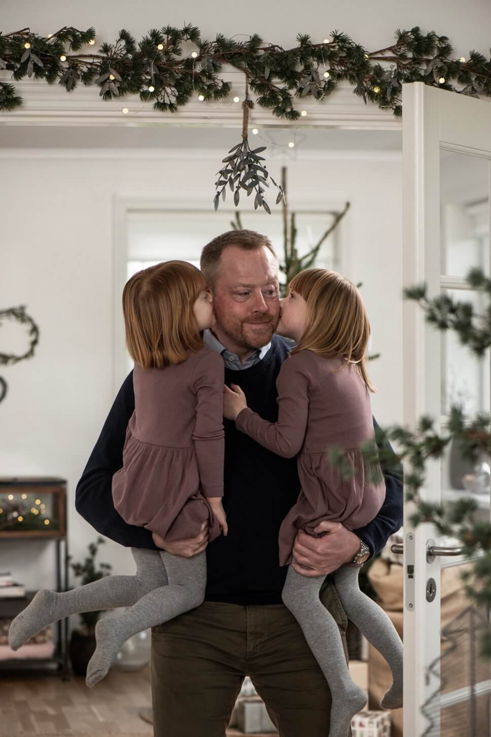 Zwei Kinder küssen ihren Vater unterm Mistelzweig