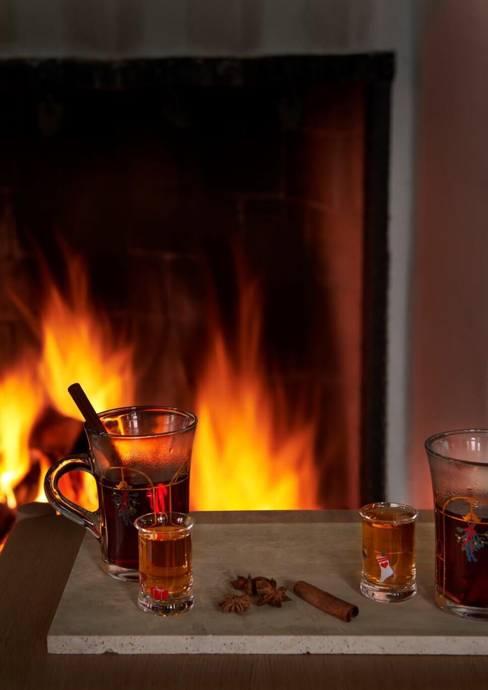 Gefüllte Punsch- und Schapsgläser stehen auf Tisch vor brennendem Kamin