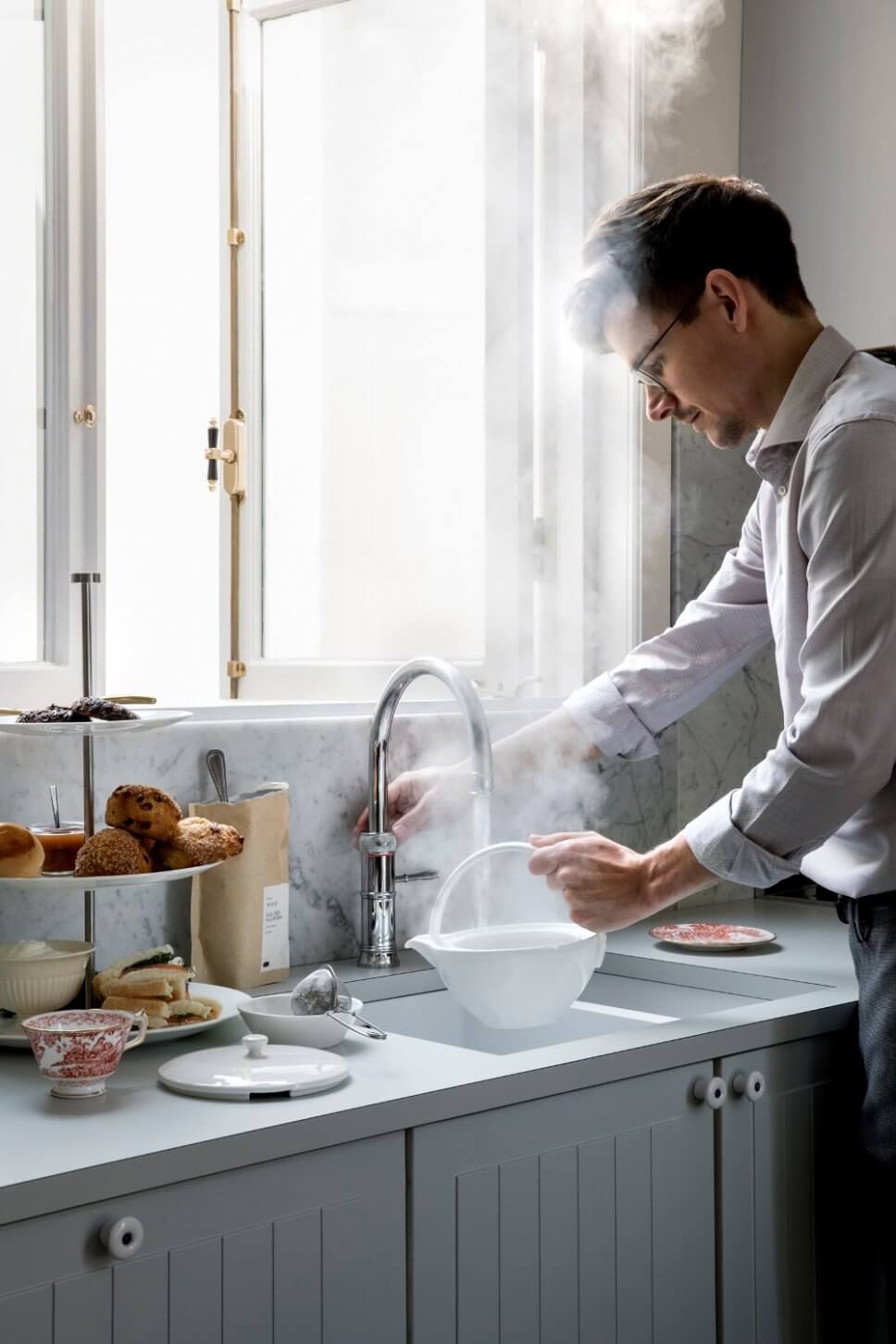 Mann gießt kochend heißes Wasser aus Wasserhahn in Teekanne in Küche