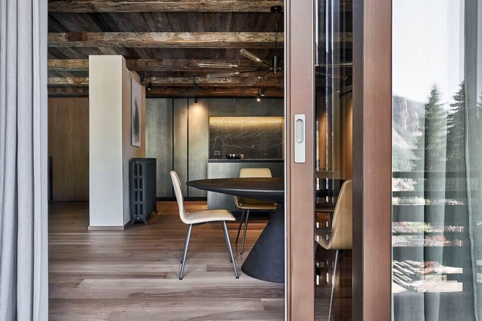 Minimalistisch eingerichteter offener Wohnraum mit Esstisch und Stühlen udn offener Küche im modernen Chalet-Stil