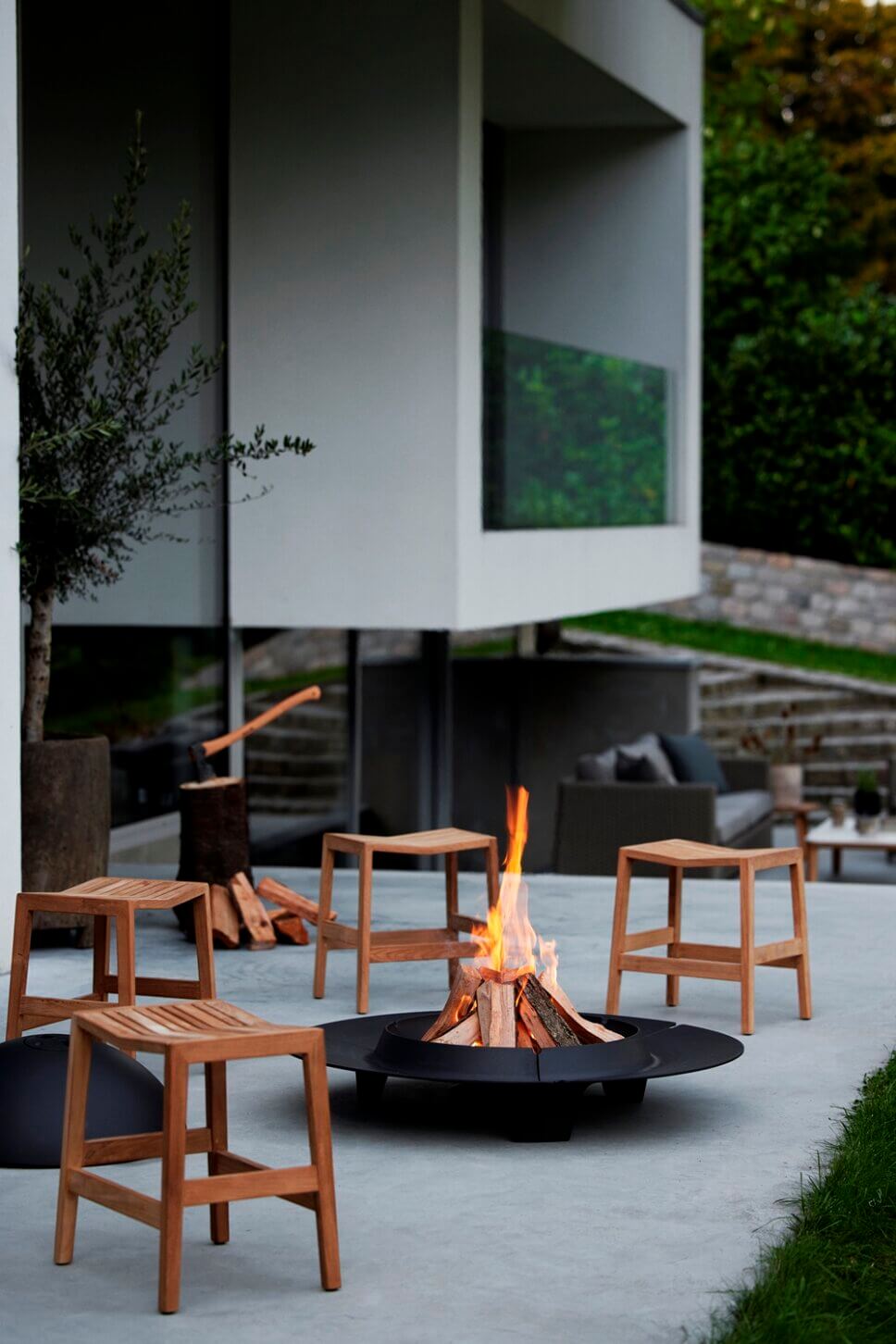 Holzhocker stehen um brennden Feuerschale auf der Terrasse
