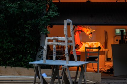 Stuhl aus Ästen steht vor beleuchteter Werkstatt mit moderner Fräse