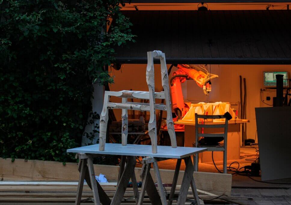 Stuhl aus Ästen steht vor beleuchteter Werkstatt mit moderner Fräse