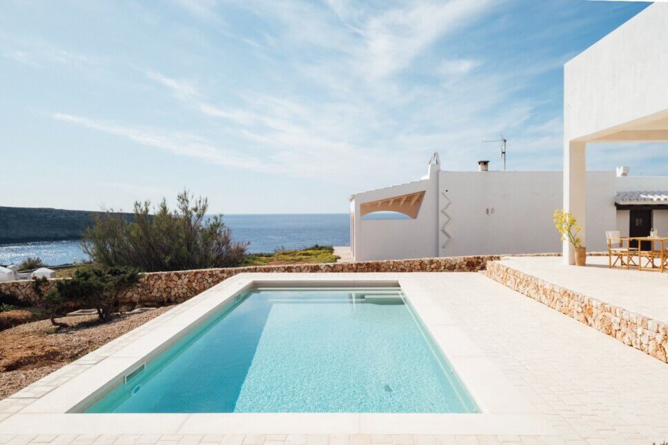 Weiße kleine, mediterrane Villa mit Korbstühlen auf Terrasse und Swimmingpool