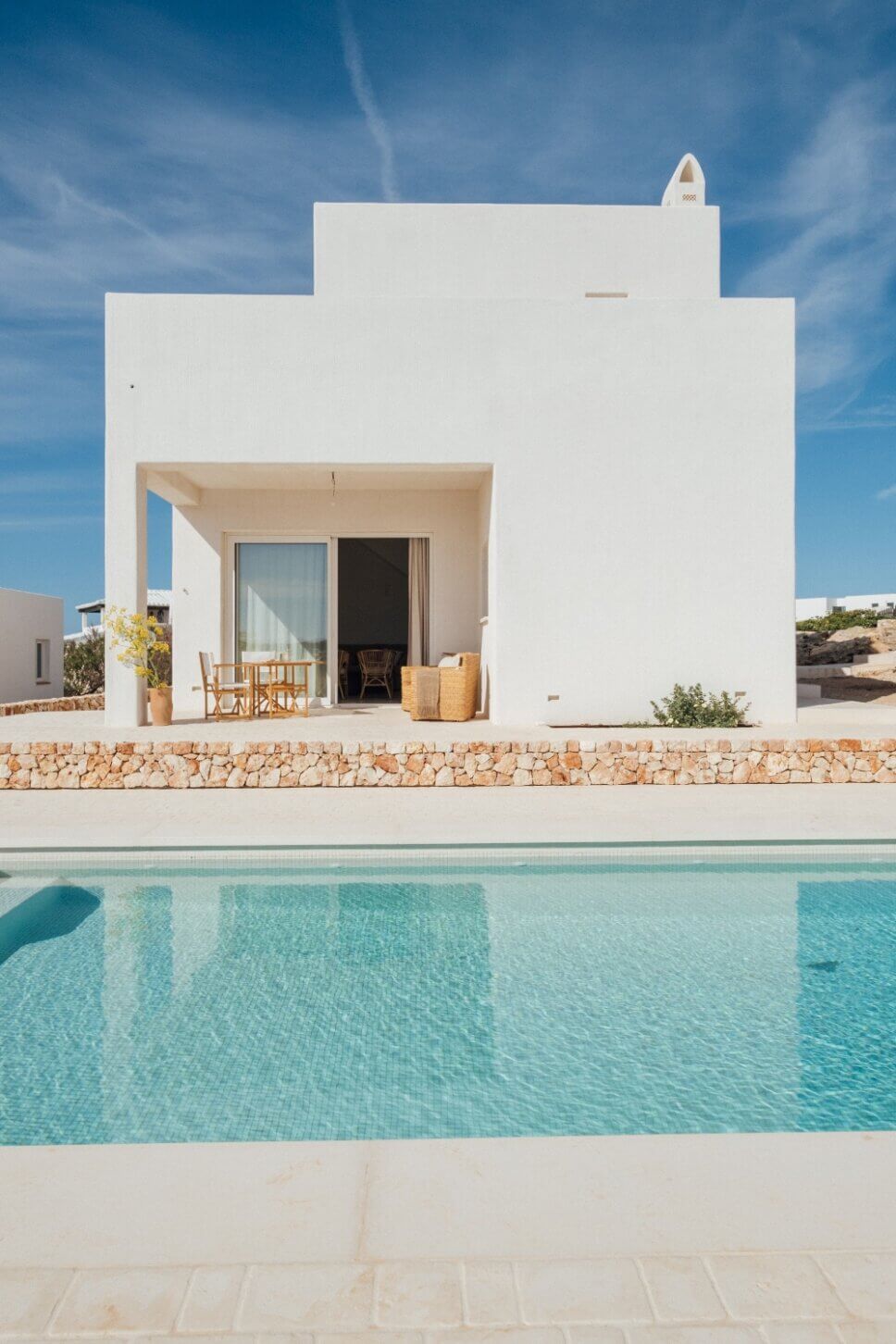 Weiße kleine, mediterrane Villa mit Korbstühlen auf Terrasse und Swimmingpool