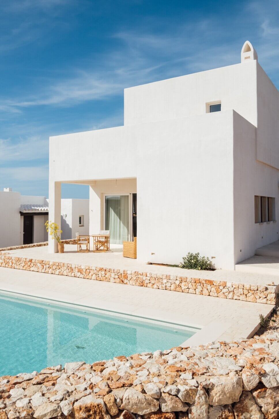 Weiße kleine, mediterrane Villa mit Korbstühlen auf Terrasse und Swimmingpool