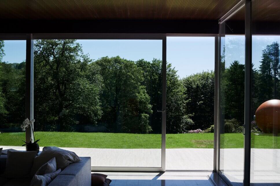 Offenes Wohnzimmer in moderner Villa aus den 60er Jahren mit großer Fensterfront und Blick in den Garten