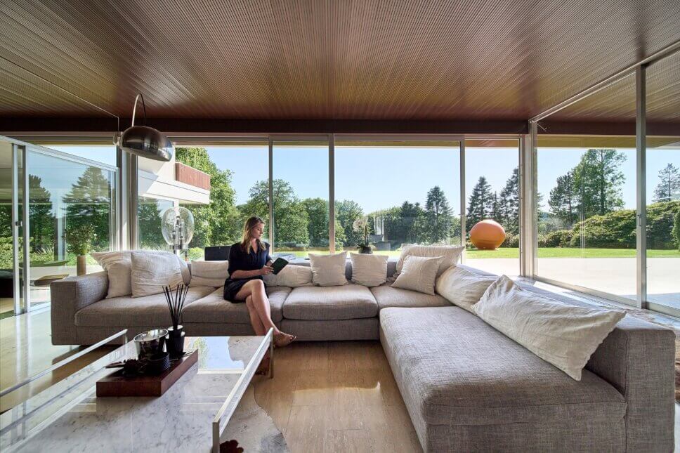 Offenes Wohnzimmer in moderner Villa aus den 60er Jahren mit großer Fensterfront und Blick in den Garten