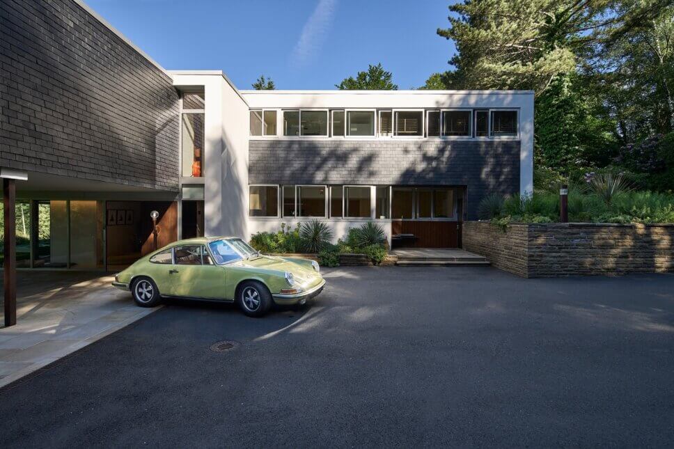 Moderne Villa aus den 60er Jahren mit großer Fensterfront und einem Porsche 911 im Vordergrund