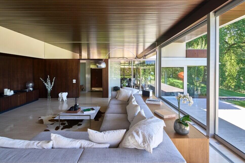 Offenes Wohnzimmer in moderner Villa aus den 60er Jahren mit großer Fensterfront und Blick in den Garten