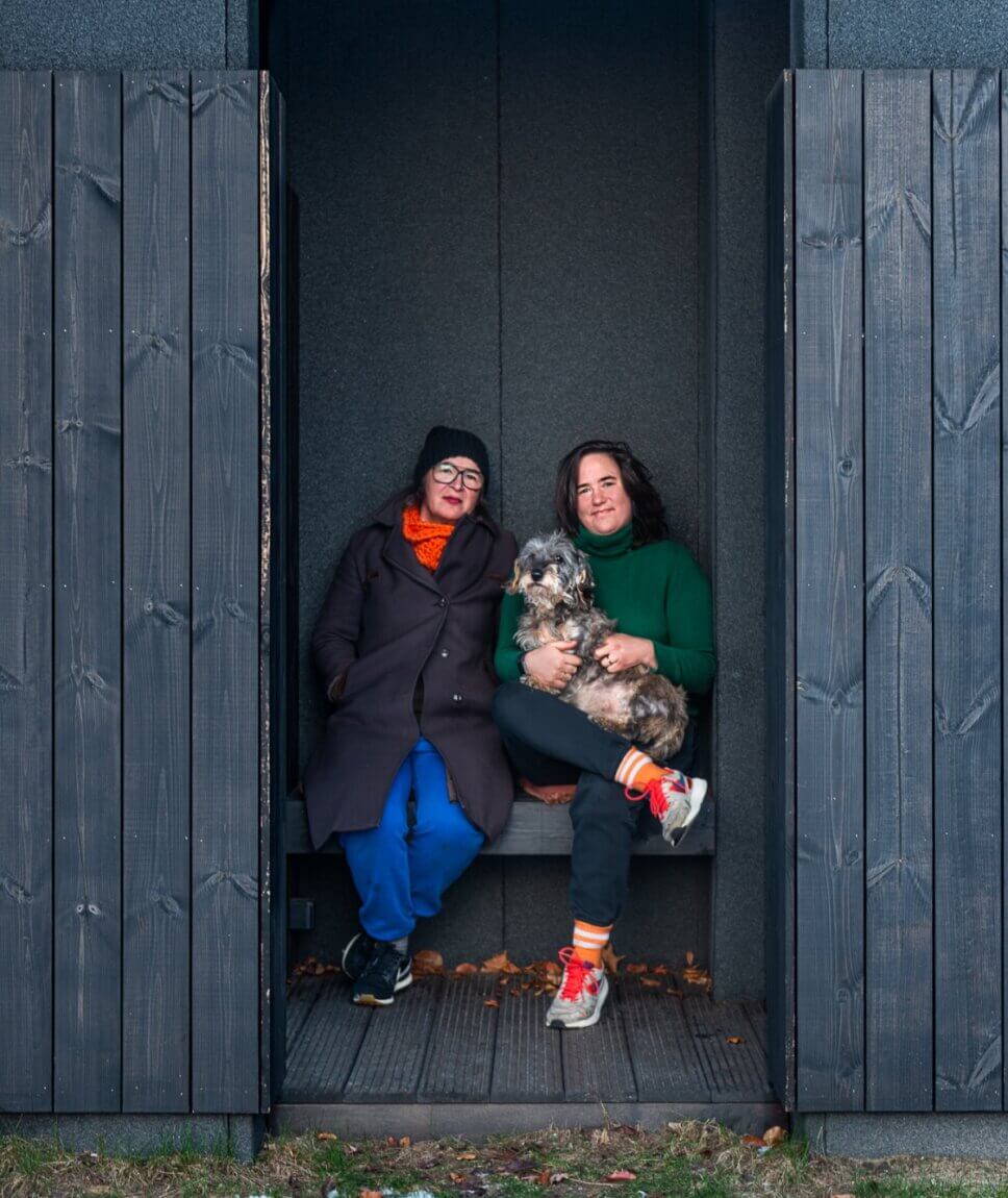 Zwei Frauen sitzen mit einem Hund in der Nische einer Veranda