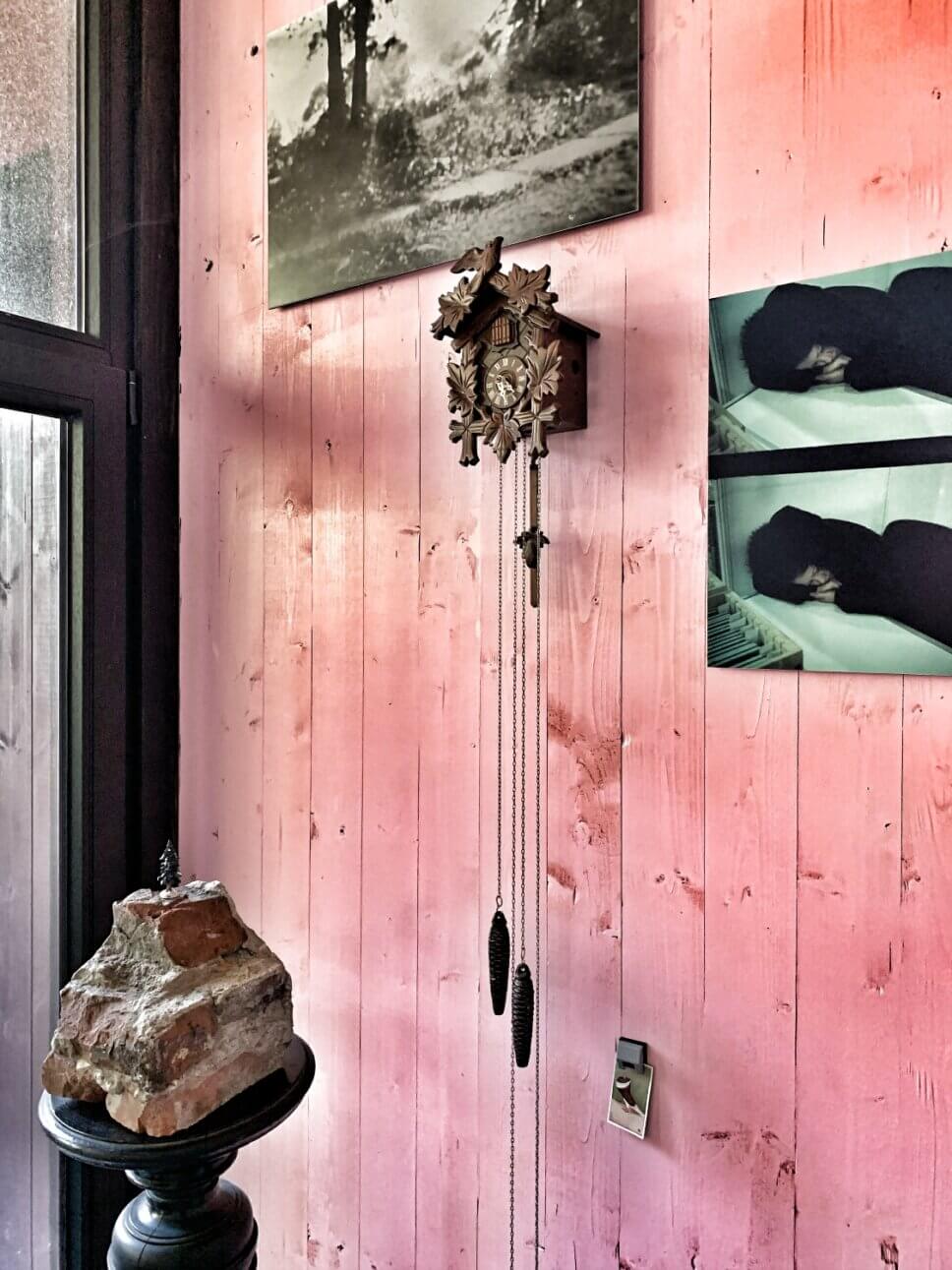 Raue rosa gestrichene Holzwand mit Bildern und Kuckucksuhr