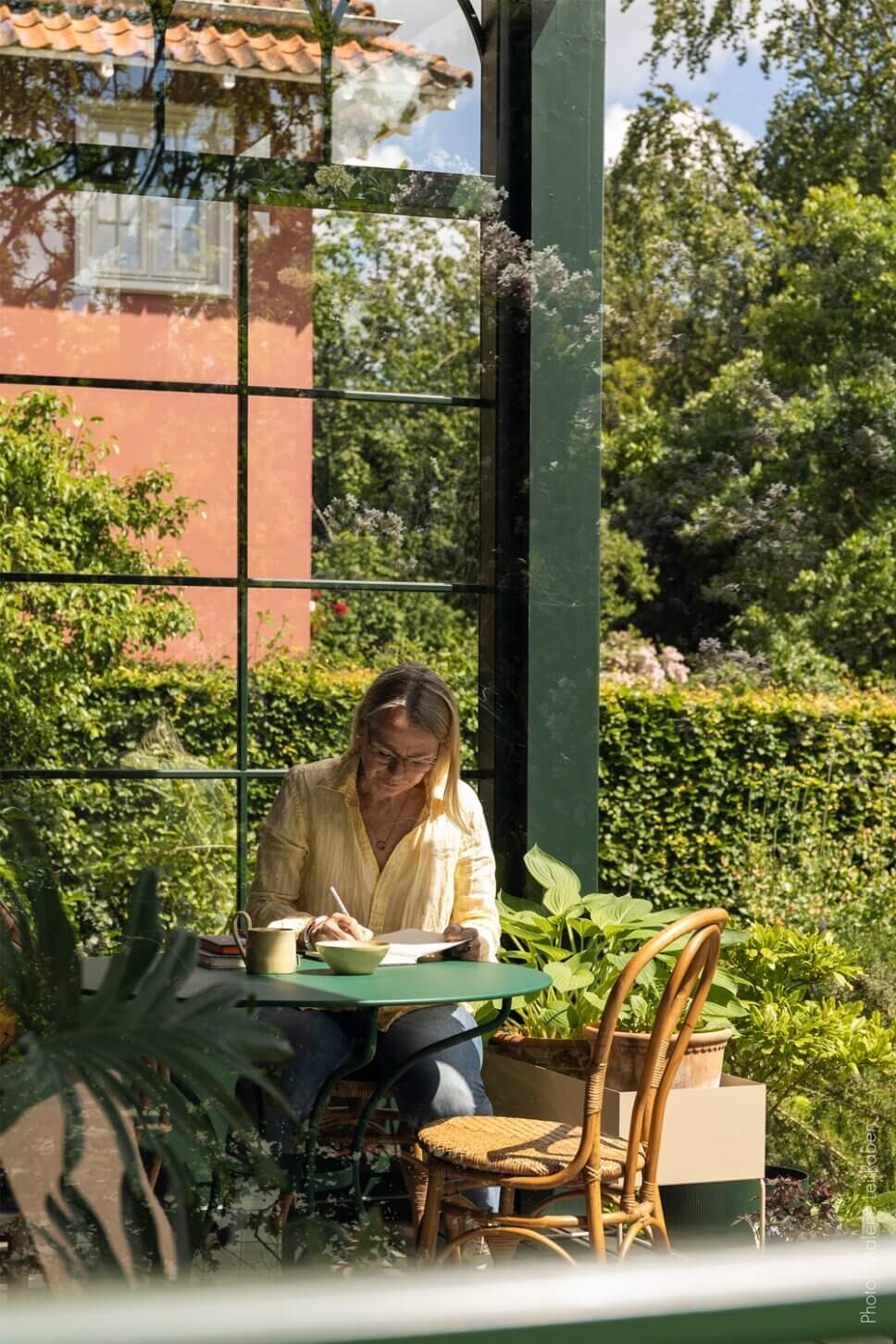 Behaglich mit Korbsofa und Esstisch eingerichtete Veranda einer alten Villa mit großem Garten. Eine Vase mit üppigem Blumenstrauß steht auf dem Tisch