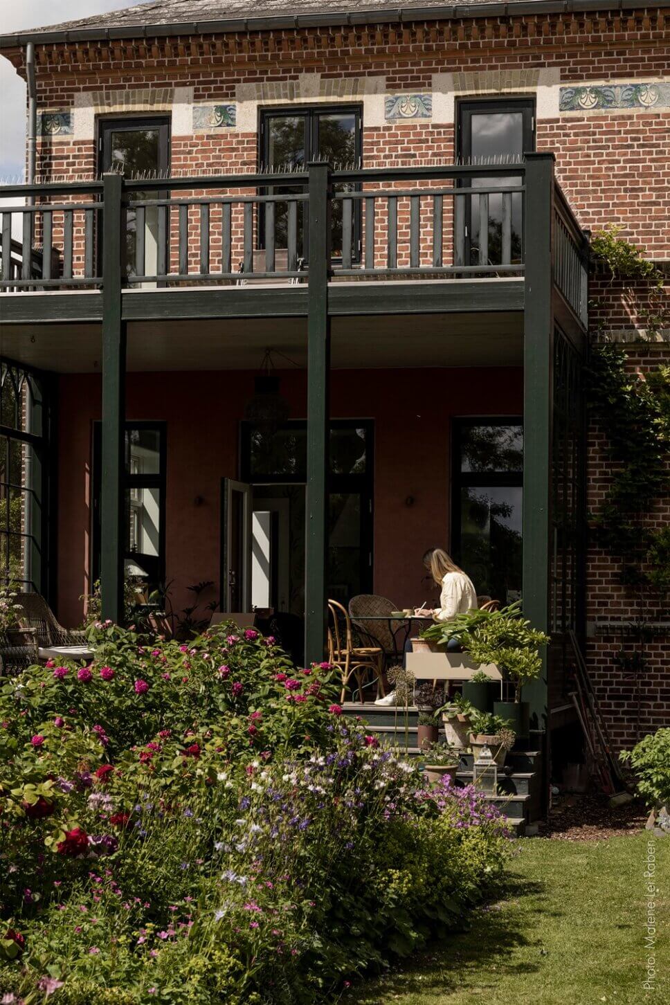 Behaglich mit Korbsofa und Esstisch eingerichtete Veranda einer alten Villa mit großem Garten. Eine Vase mit üppigem Blumenstrauß steht auf dem Tisch