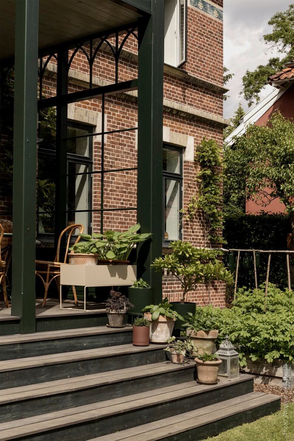 Behaglich mit Korbsofa und Esstisch eingerichtete Veranda einer alten Villa mit großem Garten. Eine Vase mit üppigem Blumenstrauß steht auf dem Tisch