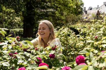 Frau schneidet an Rosenstock in blühendem Garten