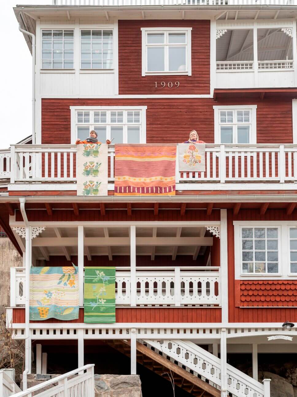 Frauen hängen farbenfrohe Teppiche von Balkonen einer skandinavischer Altbau Villa