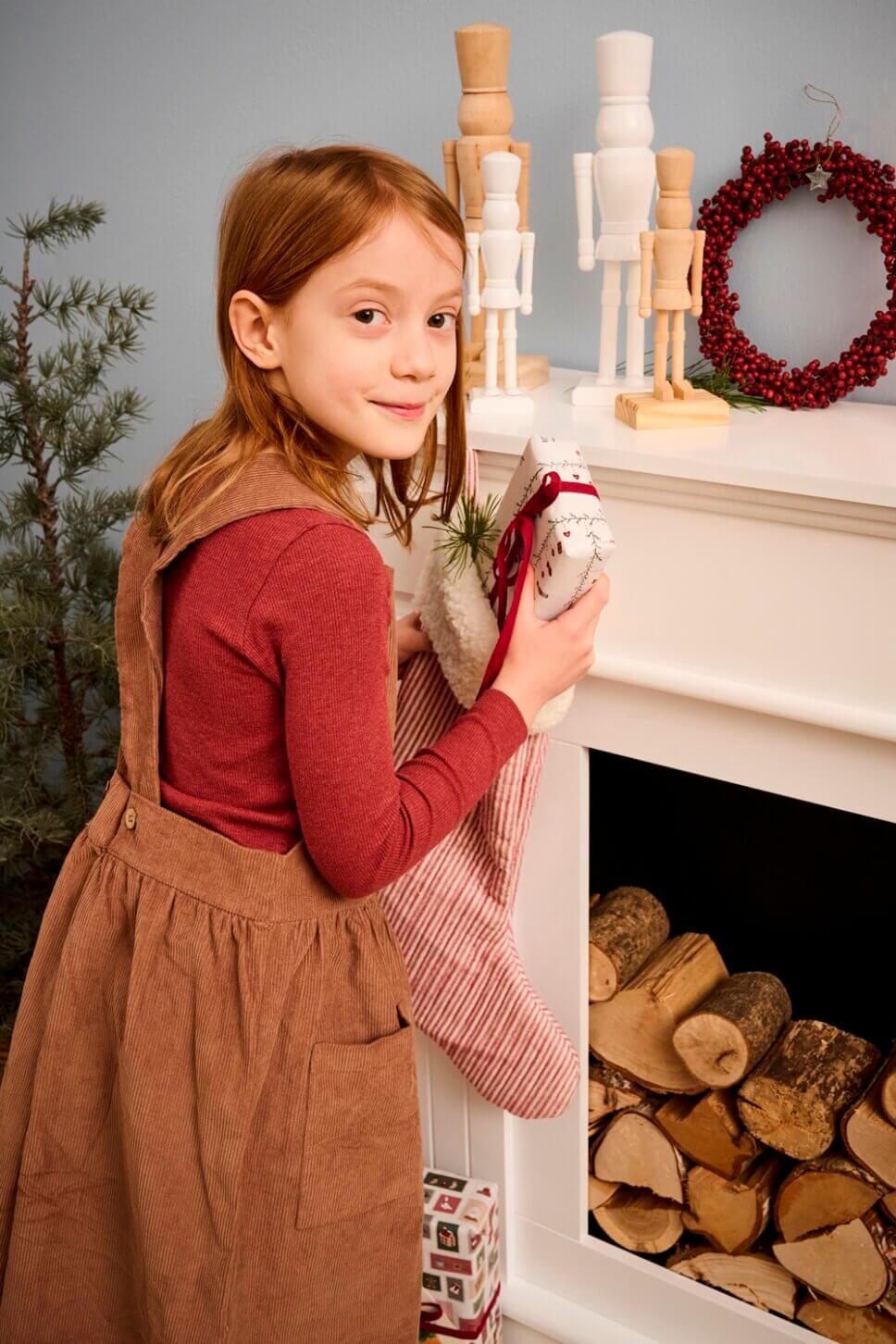 Mädchen holt Geschenk aus Weihnachtstrumpf im mit Weihnachtsdeko geschmückten Altbau