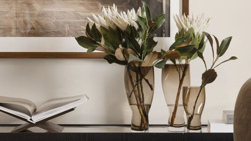 Blumen in rauchbrauner Glasvasen auf Konsole