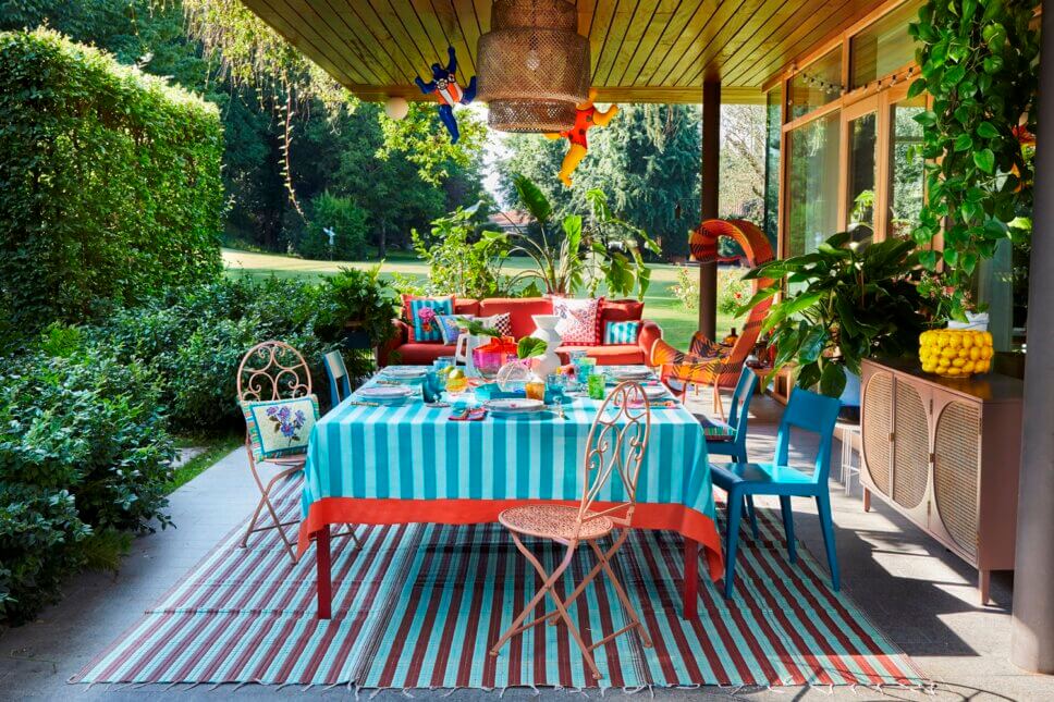 Behaglich mit farbenfrohen Stoffen und Designklassikern modern eingerichtete Terrasse mit liebevoll gedecktem Tisch an italienischem Bungalow