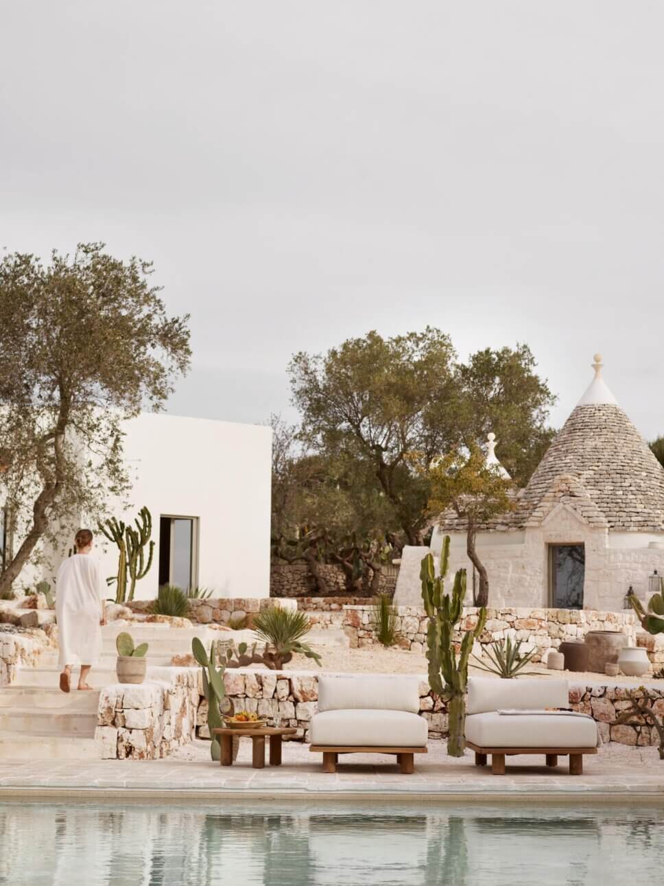 Mediterranes weißes Haus und Trullo mit Holz-Gartenmöbeln auf der Terrasse vor Pool