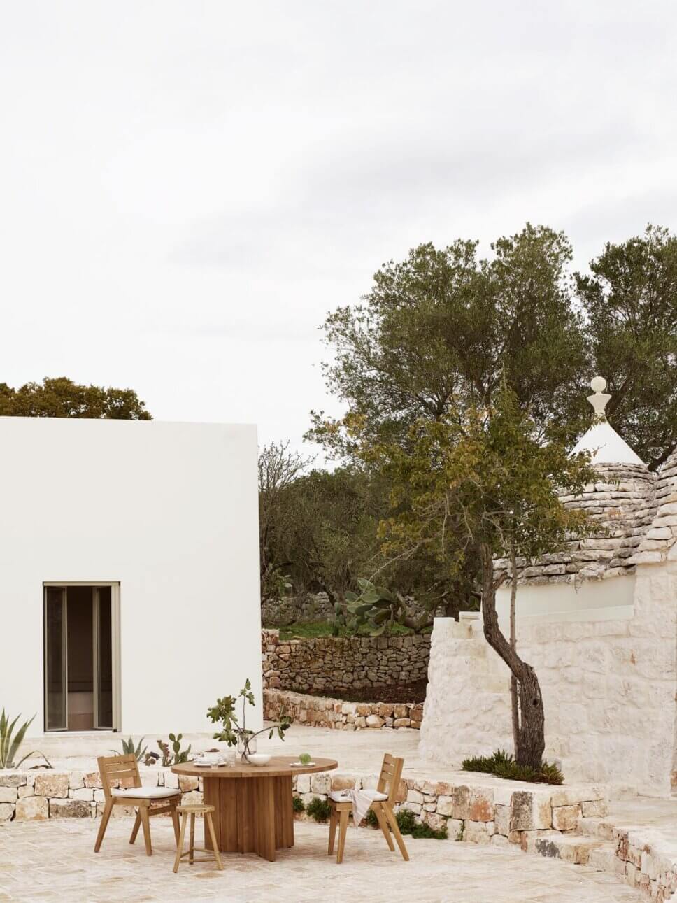Mediterranes weißes Haus und Trullo mit Holz-Gartenmöbeln auf der Terrasse