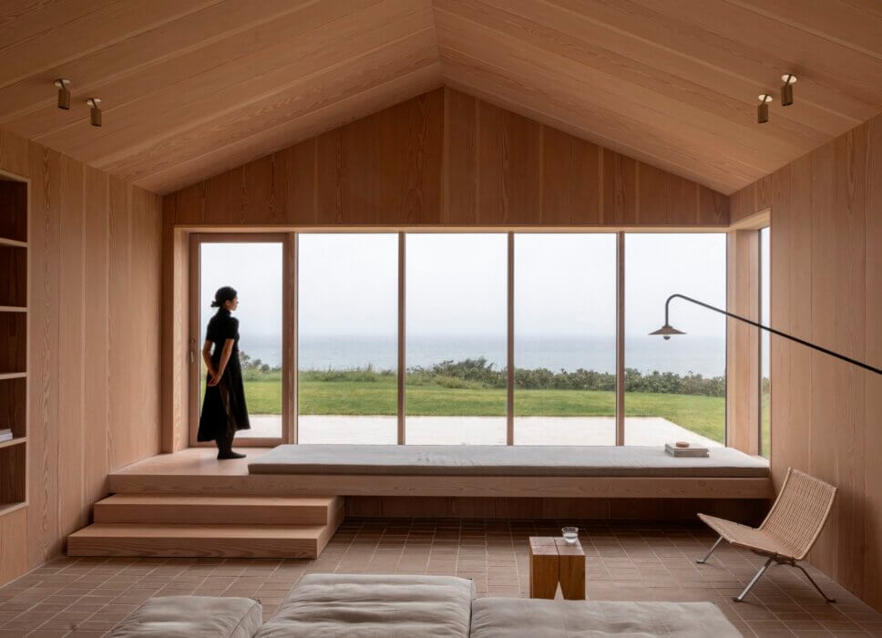 Minimalistisch eingerichtetes, mit Holz vertäfeltes Wohnzimmer in Architektenhaus mit Panoramafenster und Meerblick